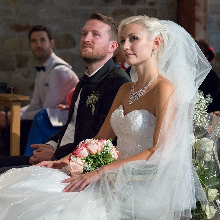 couple en tenue de mariés avec bouquet écoutant le sermon