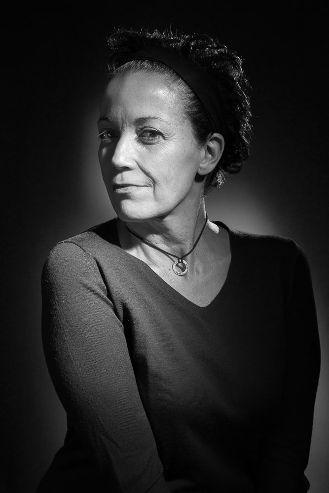 Portrait noir et blanc de la photographe, brune aux yeux marron, visage quasi de profil gauche et buste de face à 80%